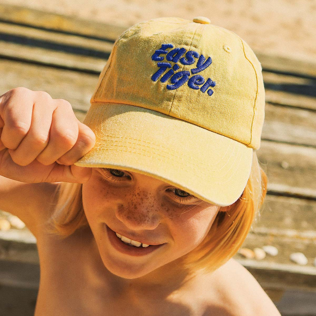 Girl pulling the brim of the Easy Tiger kids cotton cap in mustard