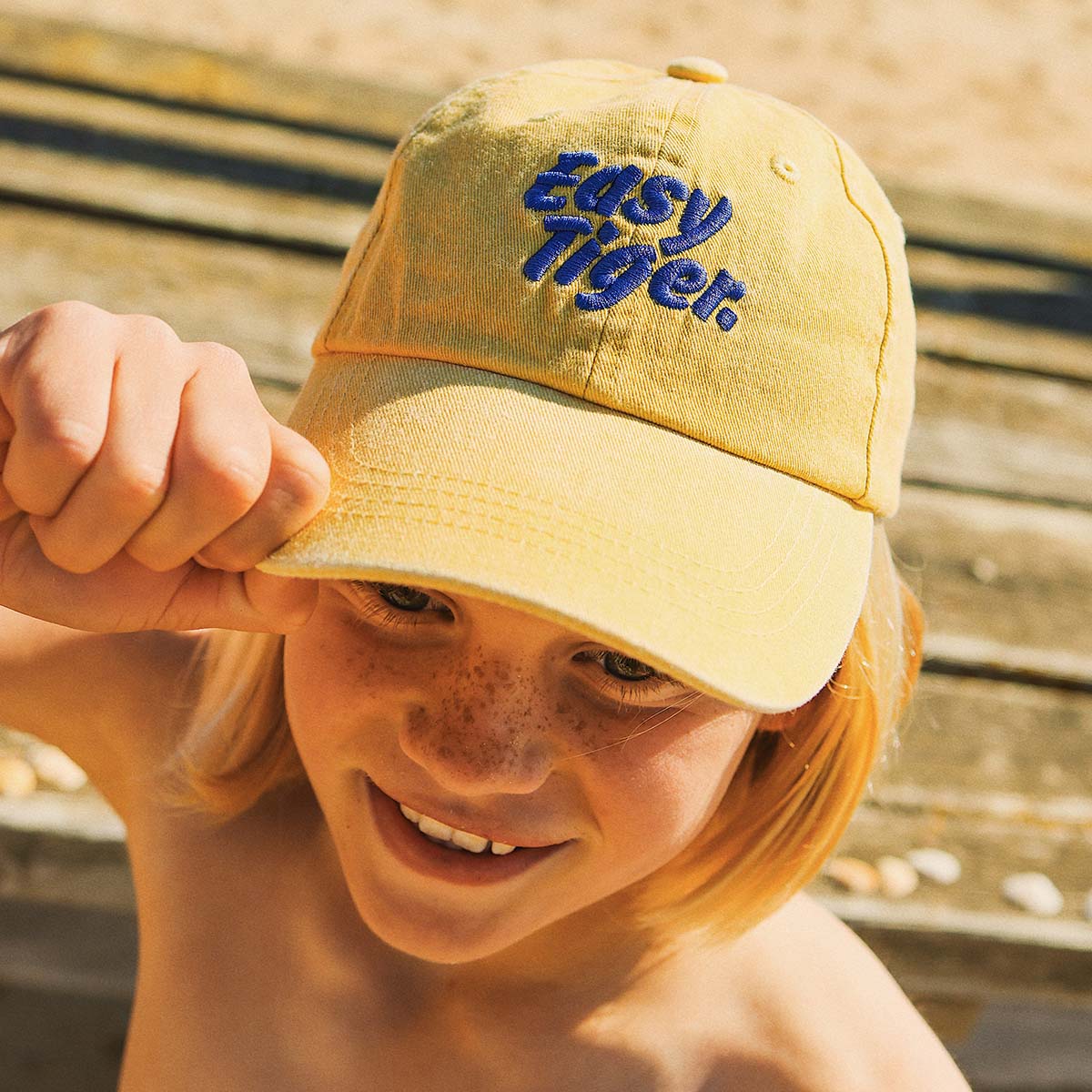 Girl pulling the brim of the Easy Tiger kids cotton cap in mustard