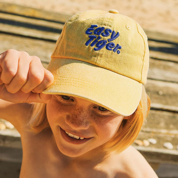 Girl pulling the brim of the Easy Tiger kids cotton cap in mustard