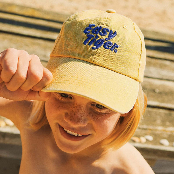 Girl pulling the brim of the Easy Tiger kids cotton cap in mustard