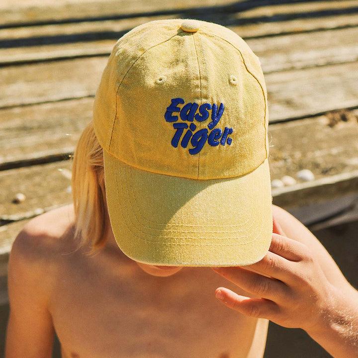 Close up of the Easy Tiger embroidery on the mustard kids cotton cap