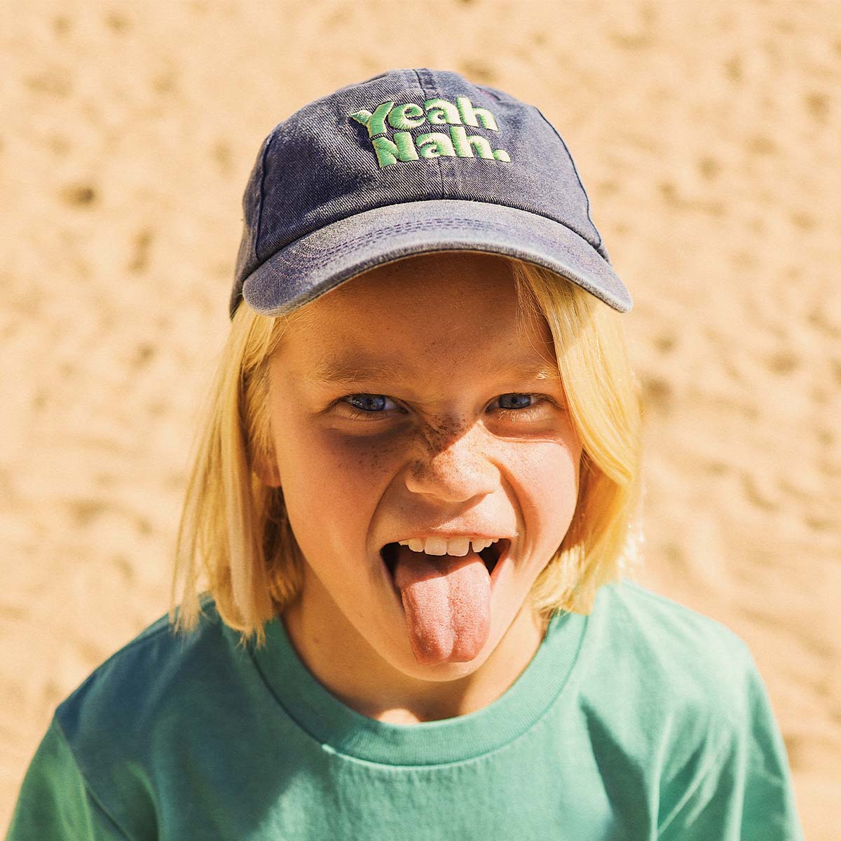 Boy pulling a face in the navy Yeah Nah kids cotton cap