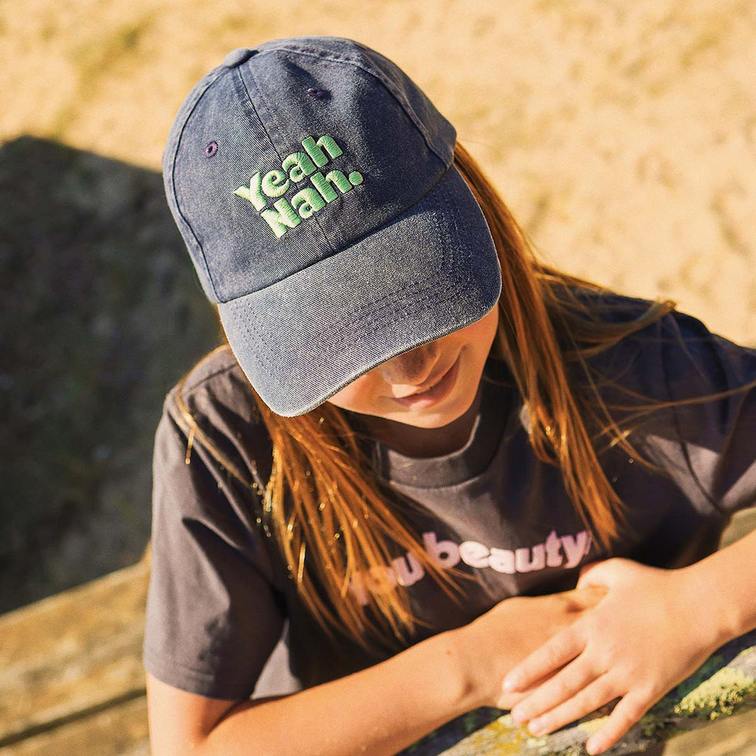 Girl sitting down in the Yeah Nah kids cotton cap in navy