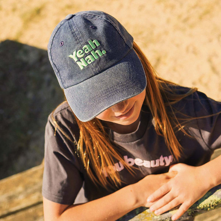 Girl sitting down in the Yeah Nah kids cotton cap in navy