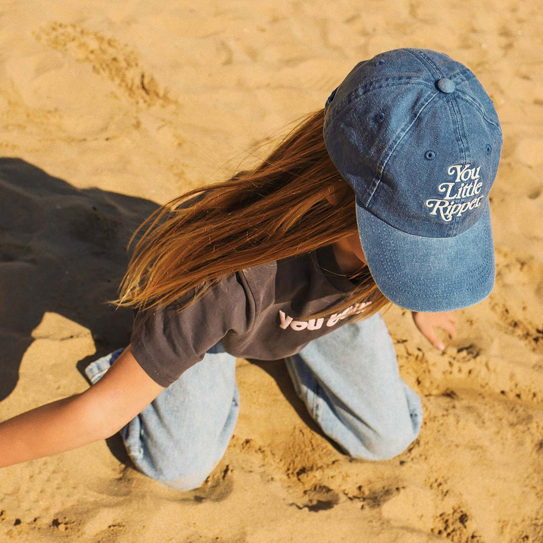 Kid lying on the sand in the blue You Little Ripper kids cotton cap