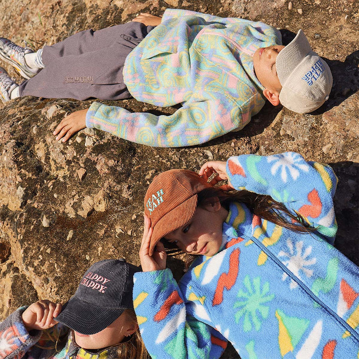 Group of kids in Skwosh cord caps lying on the rocks at the beach