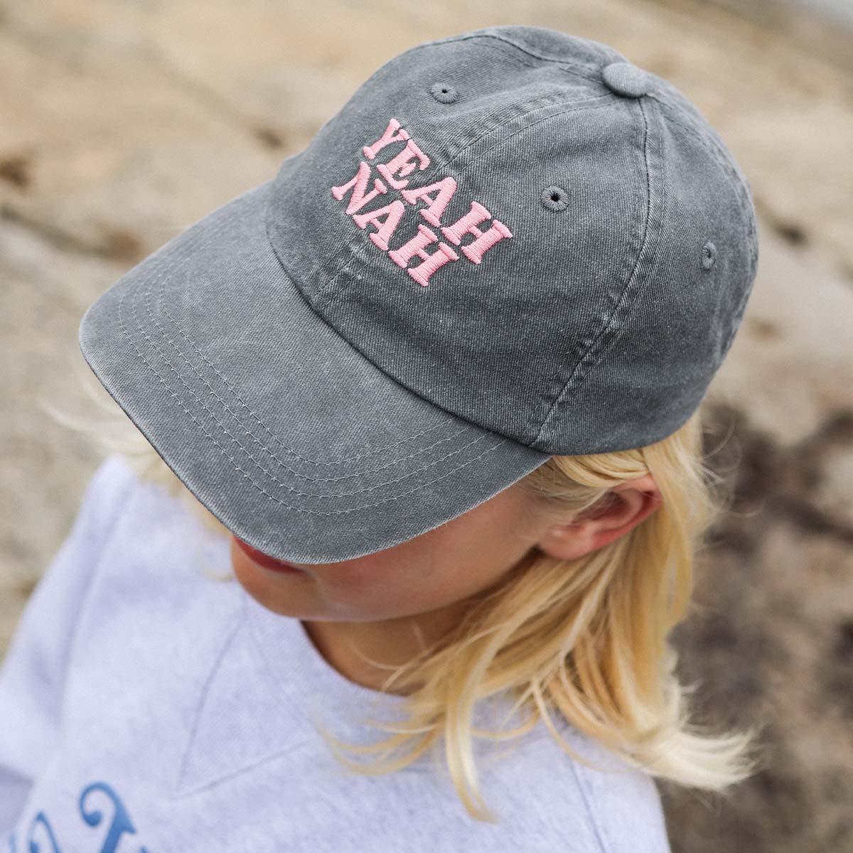 Girl at the beach wearing the Yeah Nah kids cotton cap in charcoal