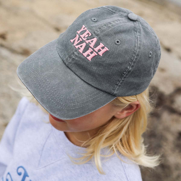 Girl at the beach wearing the Yeah Nah kids cotton cap in charcoal