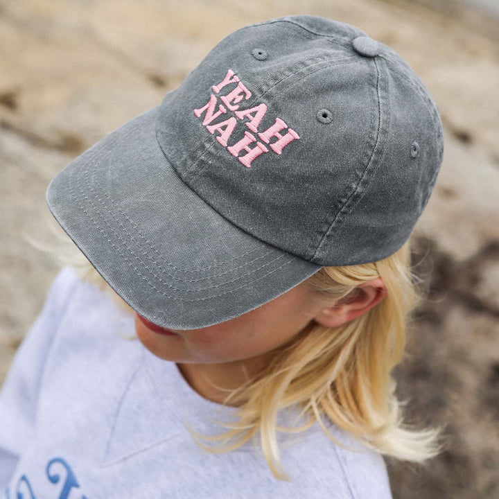 Girl at the beach wearing the Yeah Nah kids cotton cap in charcoal