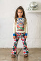 A little girl standing in a living room wearing a Rock your Baby Online Peace Long Sleeve T-Shirt and bell bottoms.