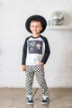 A young boy wearing a Rock your Baby Online MUSIC SPEAKS LONG SLEEVE T-SHIRT and black and white checkered pants.