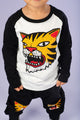 A young boy wearing a black and white TIGER RAGLAN T-SHIRT by Rock your Baby Online and black pants.