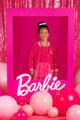 A girl is posing in front of a pink BARBIE SEQUIN JACKET frame with balloons.
