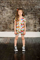 A little girl standing on a wooden floor in a BUTTERFLIES T-SHIRT by Rock your Baby Online, wearing colorful floral shorts.
