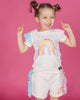 A little girl wearing a Rock your Baby Online Rainbow Dreams T-Shirt and shorts.