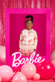 A young girl is standing in front of a pink CREAM BARBIE SWEATSHIRT frame with balloons from Rock your Baby Online.